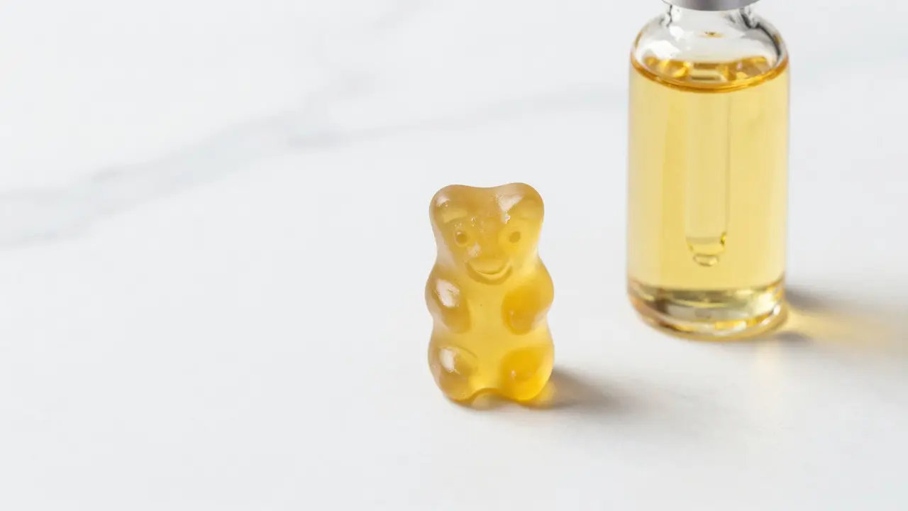 Halbiertes Gummibärchen neben einer Flasche CBD-Öl auf Marmor